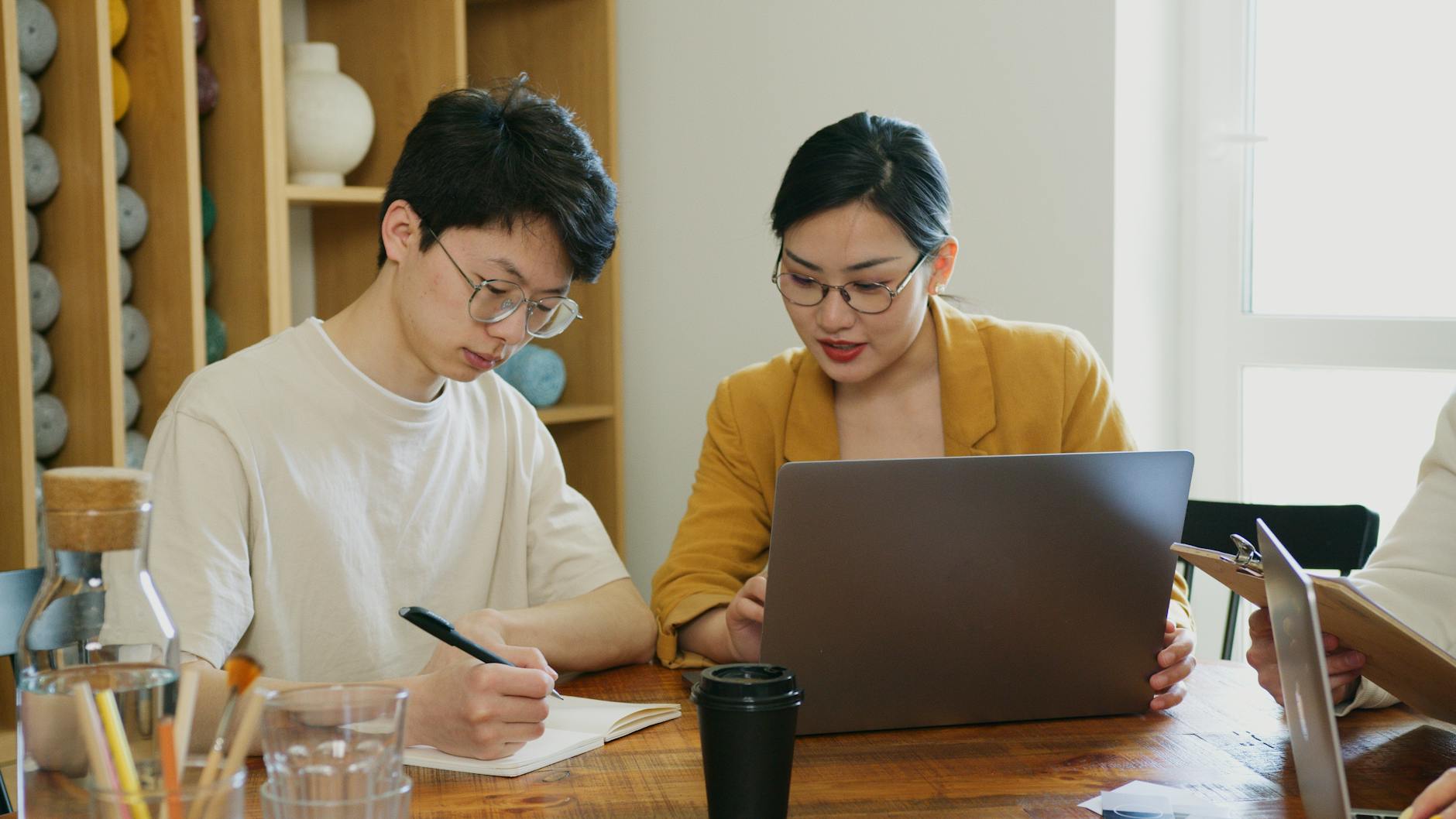 Two colleagues writing emails together at a shared laptop