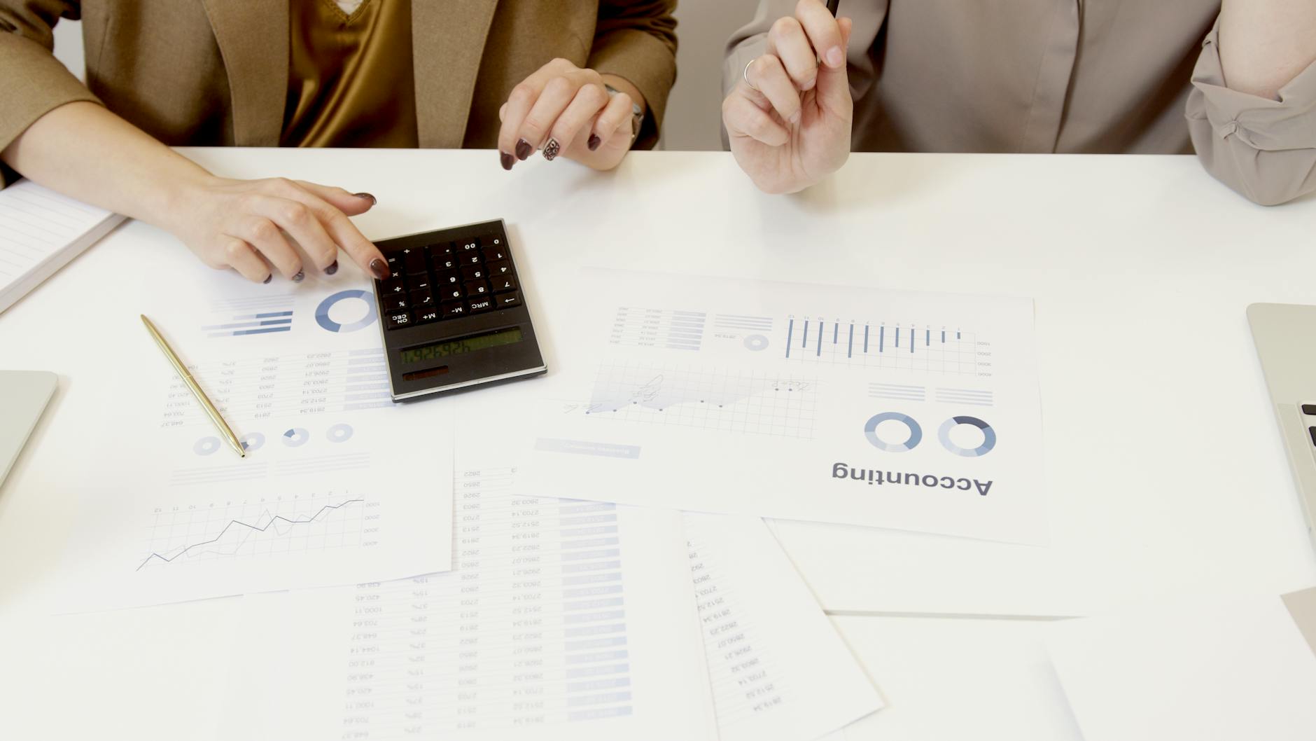 Two colleagues working through numbers on a desk, the kind of detail a Power BI measures table tidies up